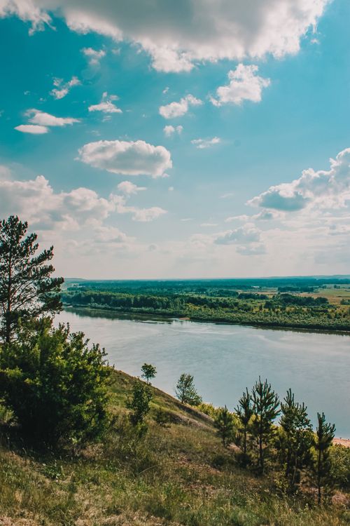 Free Beautiful scenic river landscape with lush greenery, clear blue sky, and fluffy clouds on a sunny day. Stock Photo