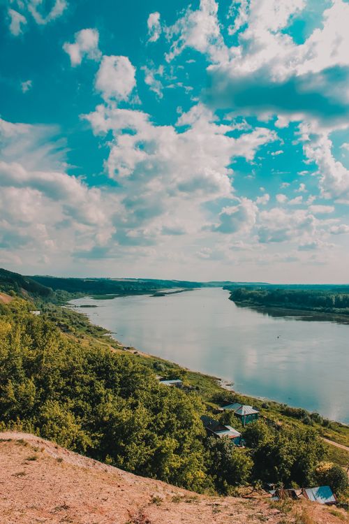 Free Breathtaking view of a winding river through a verdant countryside under a vibrant summer sky. Stock Photo