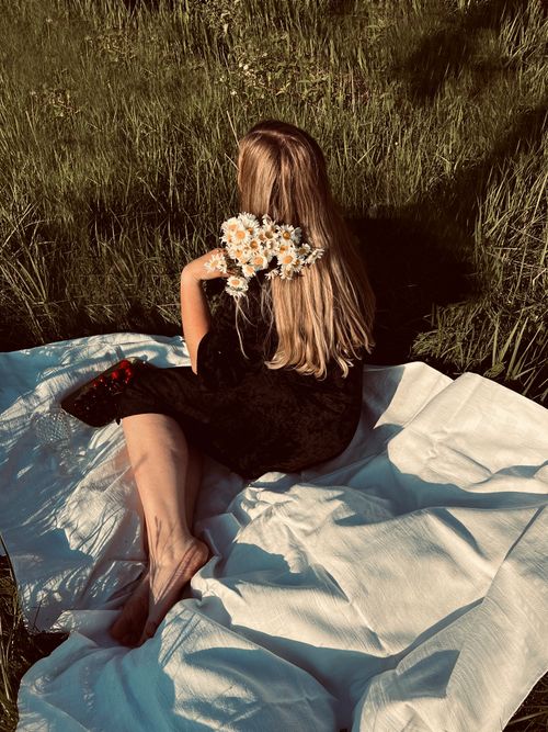 Free Blonde woman enjoying summer meadow with bouquet on a white blanket. Stock Photo