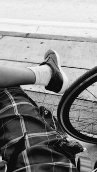 Minimalist black and white photo of a person's legs crossed near a bicycle on the street.