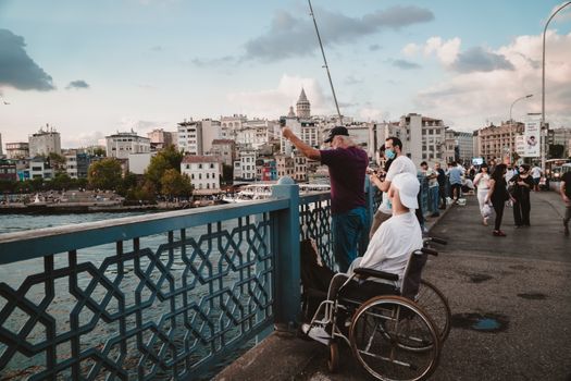 People fishing on Galata Bridge with a view of Istanbul's cityscape and Galata Tower.