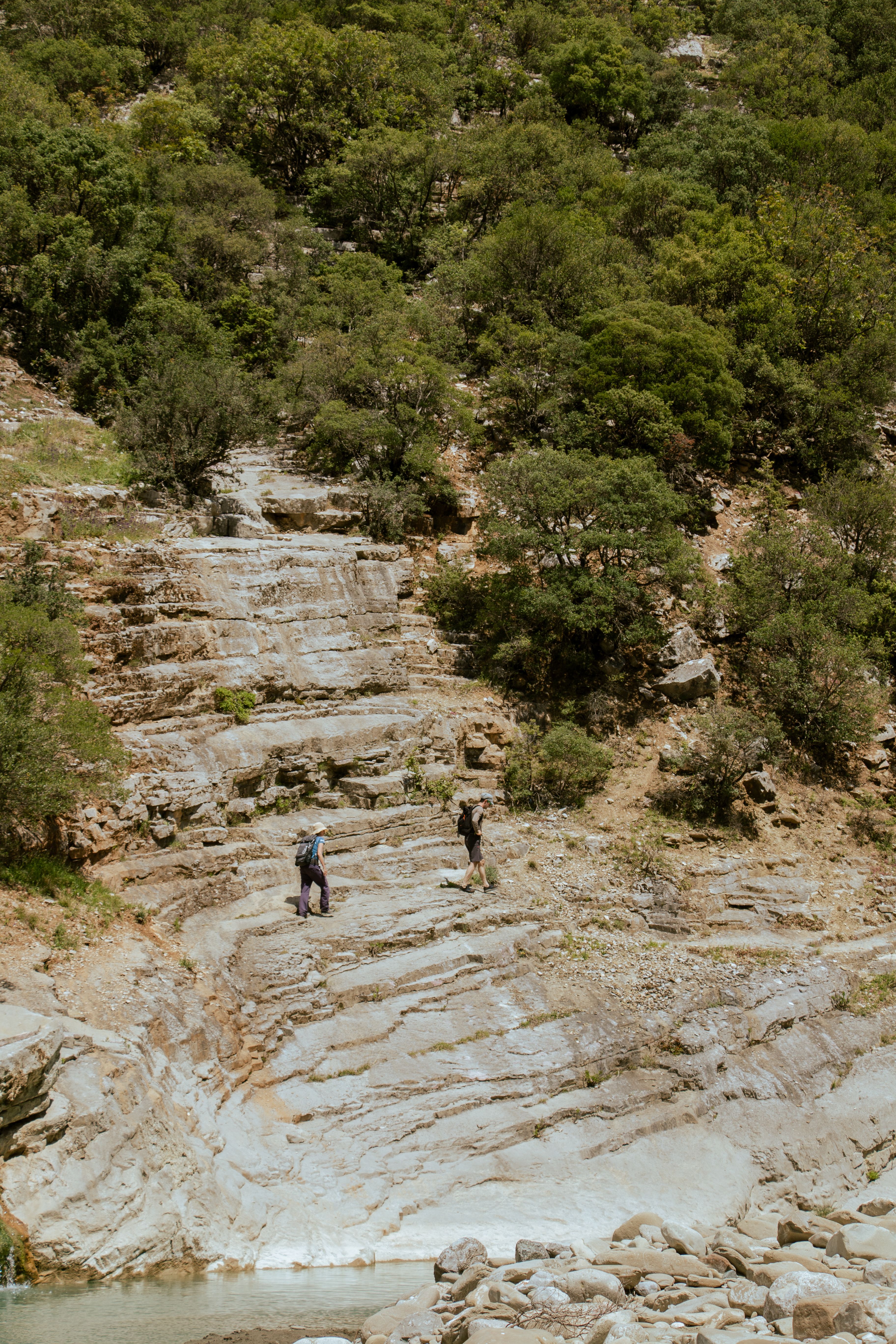 Two hikers exploring the rocky landscape in Përmet, Albania, surrounded by lush greenery.