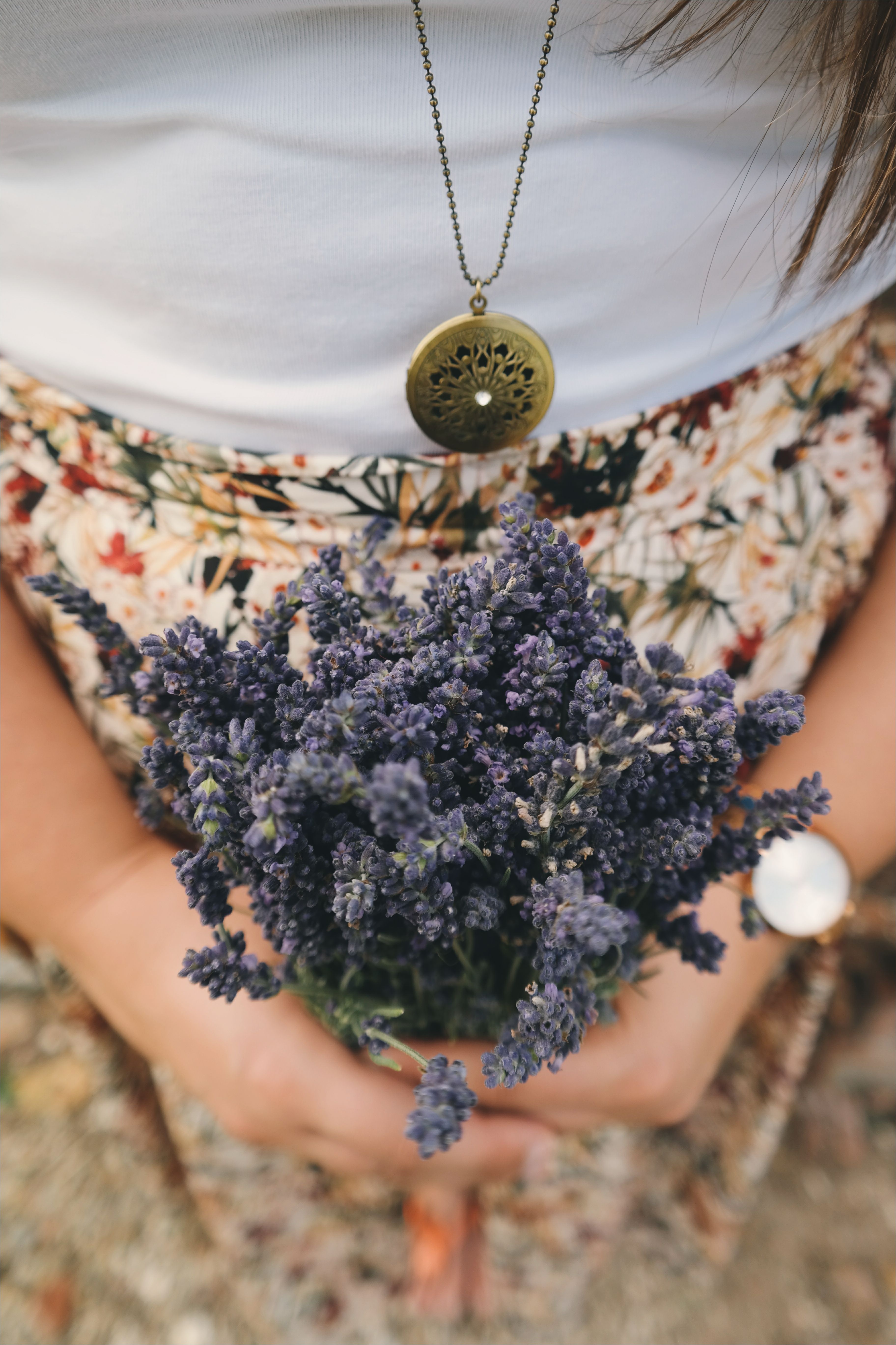 Close-up of a woman's hands holding a bouquet of lavender, wearing a floral skirt and jewelry.