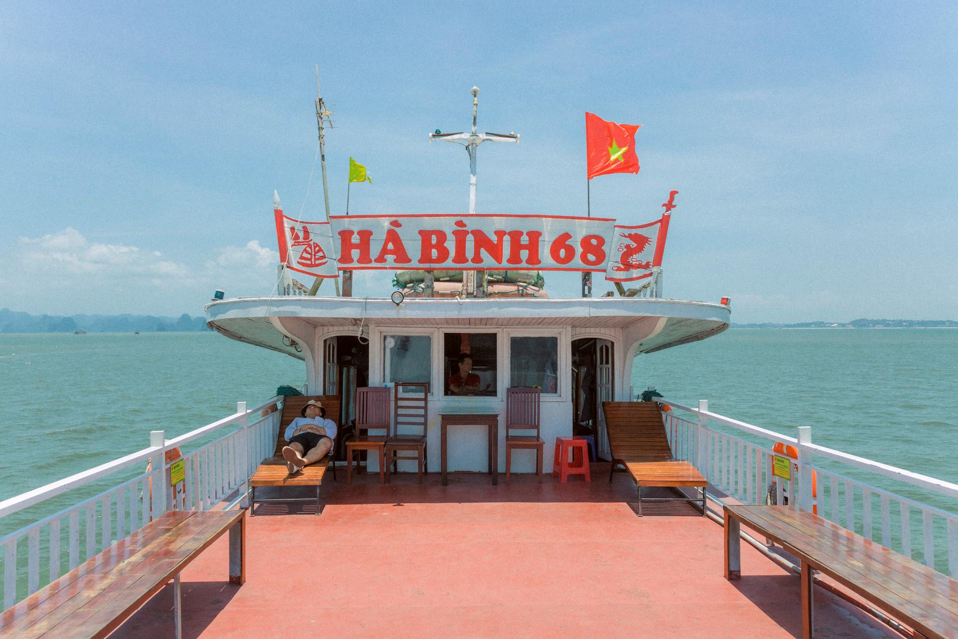 A man relaxes on a boat deck cruising through Halong Bay, Vietnam, under a clear blue sky.