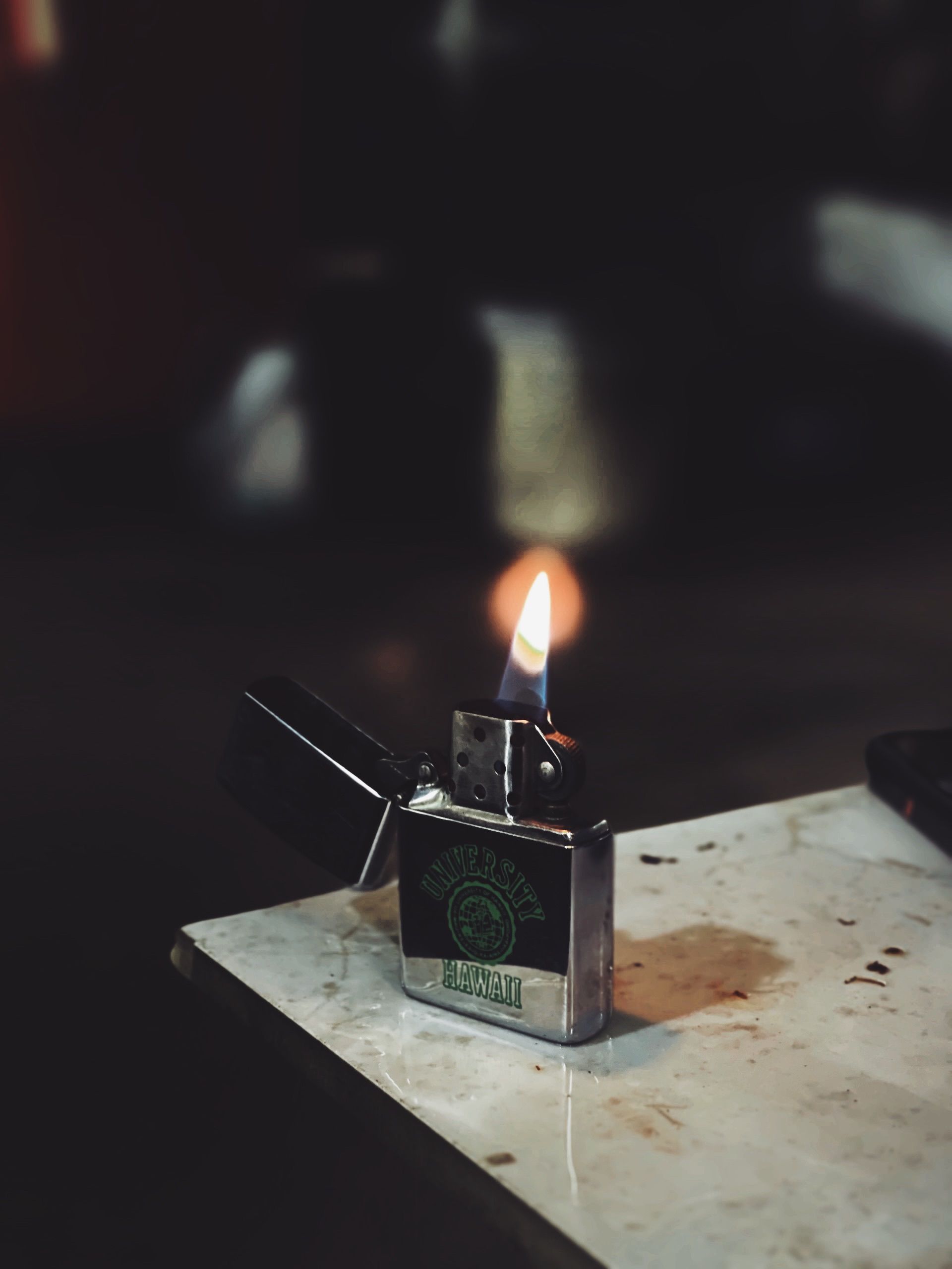 Close-up of a metal lighter with a blue and orange flame on a marble surface, evoking warmth and focus.
