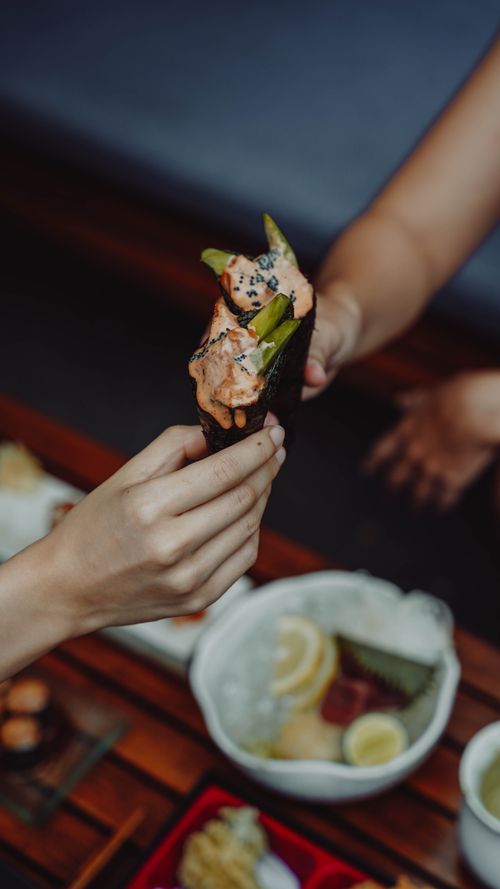 Free Hands exchanging a sushi cone at an Asian restaurant, showcasing culinary delight. Stock Photo