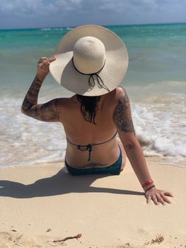 A woman in a bikini sitting on a sandy beach enjoying the serene view of the sea.