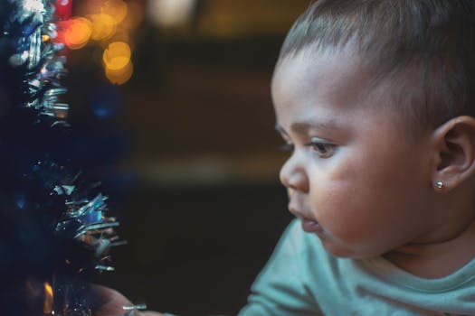 一个可爱的婴儿好奇地凝视着带有散景灯的闪闪发光的圣诞装饰品