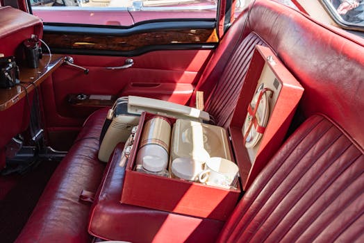 Classic red leather car interior featuring a vintage tea set on the back seat, showcasing luxury travel.