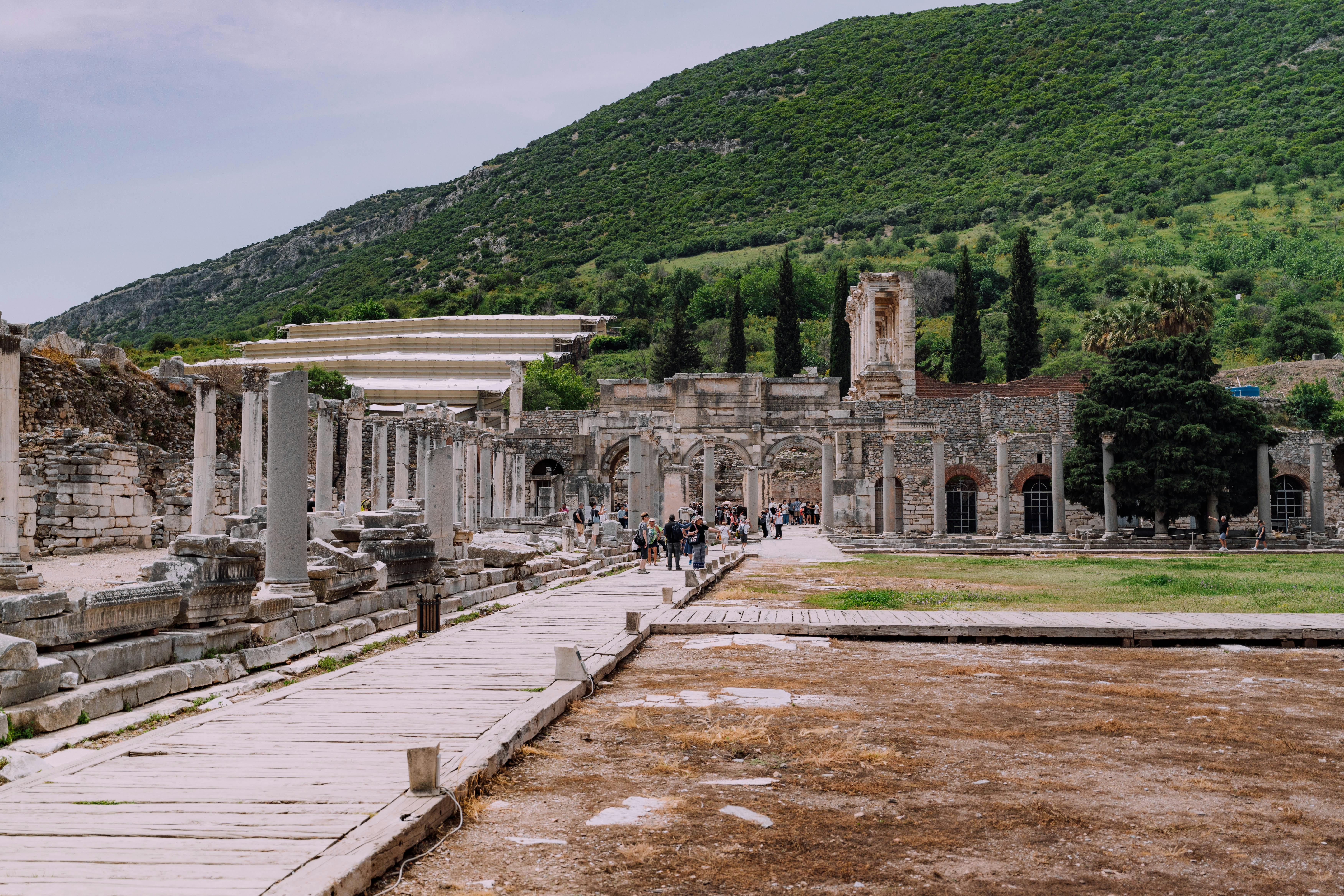 Free Tourists explore the historic ruins of Ephesus surrounded by greenery. Stock Photo