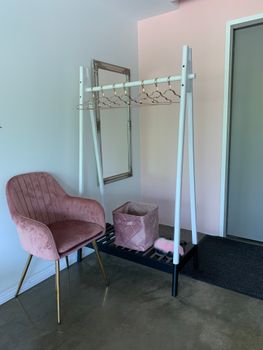 Stylish minimalist fitting room interior with a pink armchair, clothing rack, and mirror.