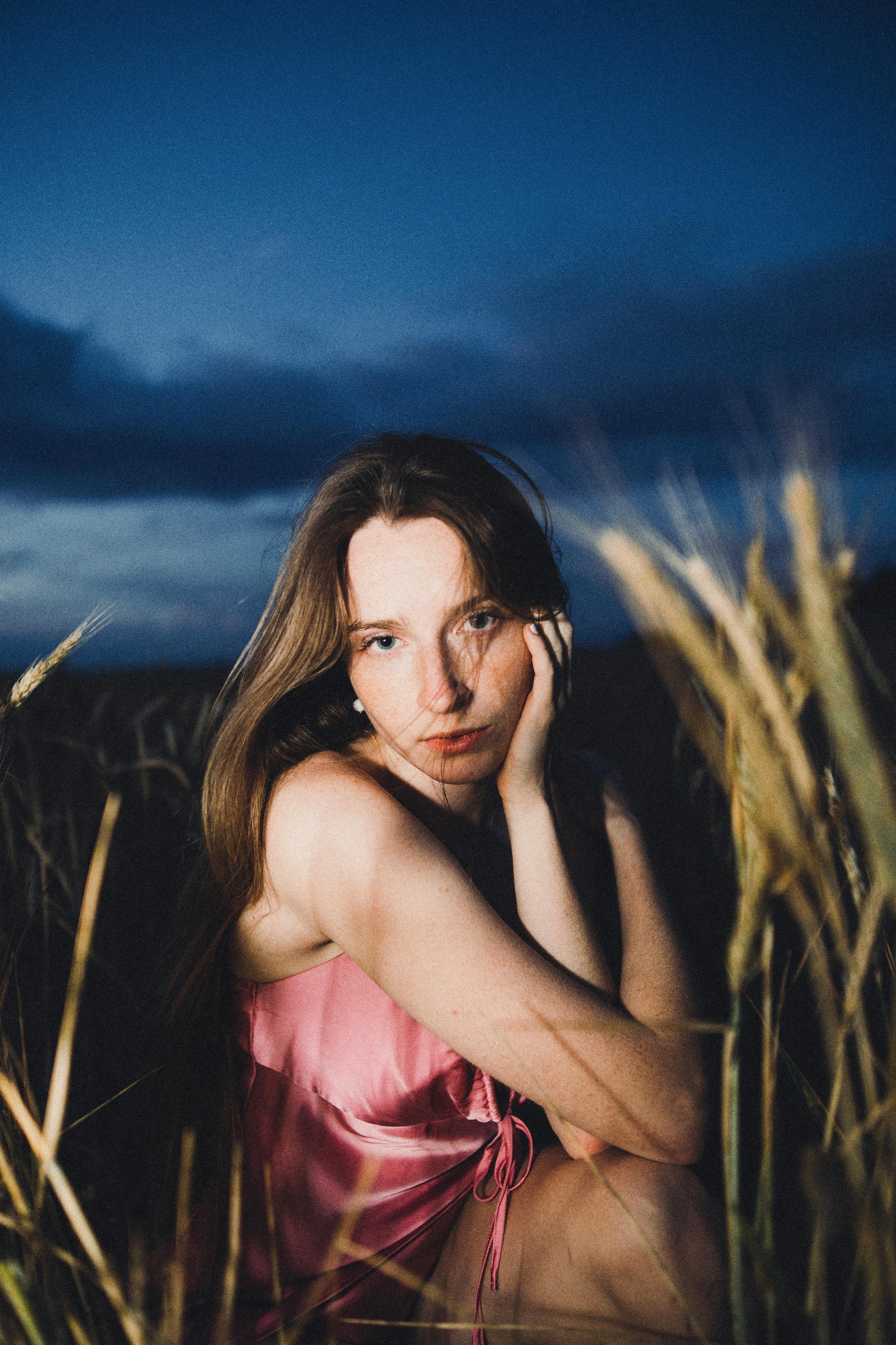 A young woman sitting in a field during twilight captured in a fashion pose.