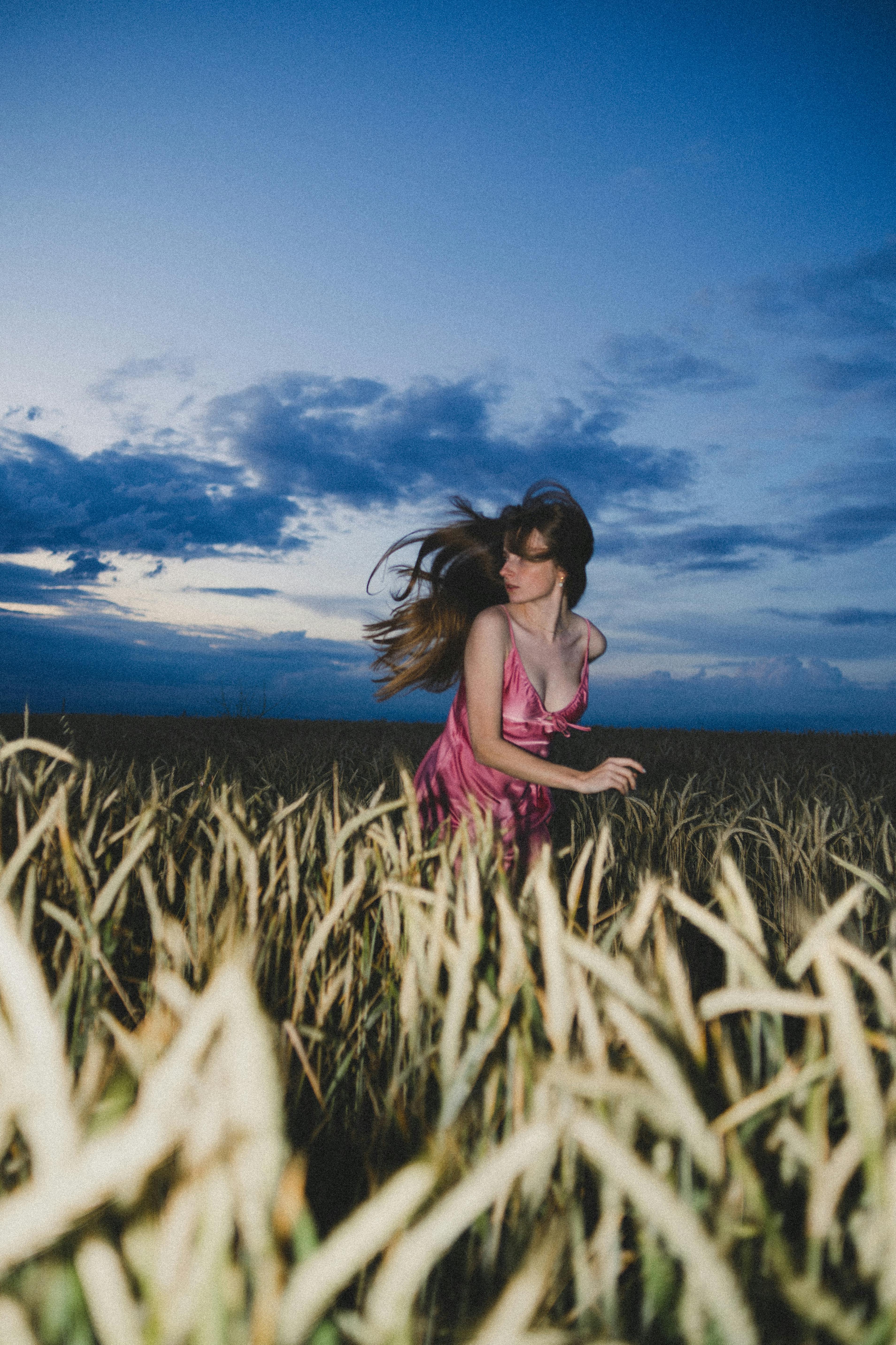 Captivating image of a young woman in a pink dress running through a wheat field at twilight.