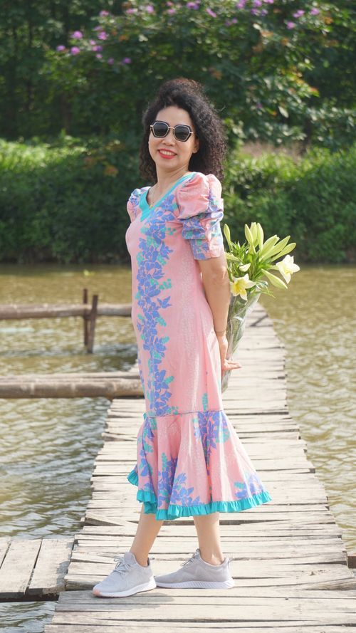 Free Smiling woman in pink floral dress holds lilies on wooden pier under summer sun. Stock Photo