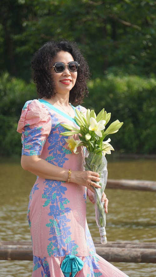 Woman in a Dress and Sunglasses Holding a Bunch of Flowers