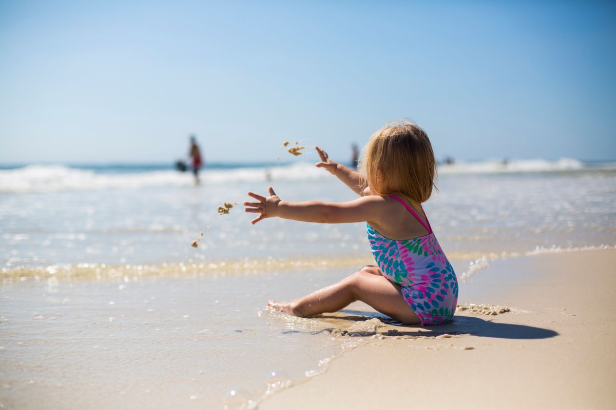 Toddler girl sitting happily on the shore at the beach on a sunny day