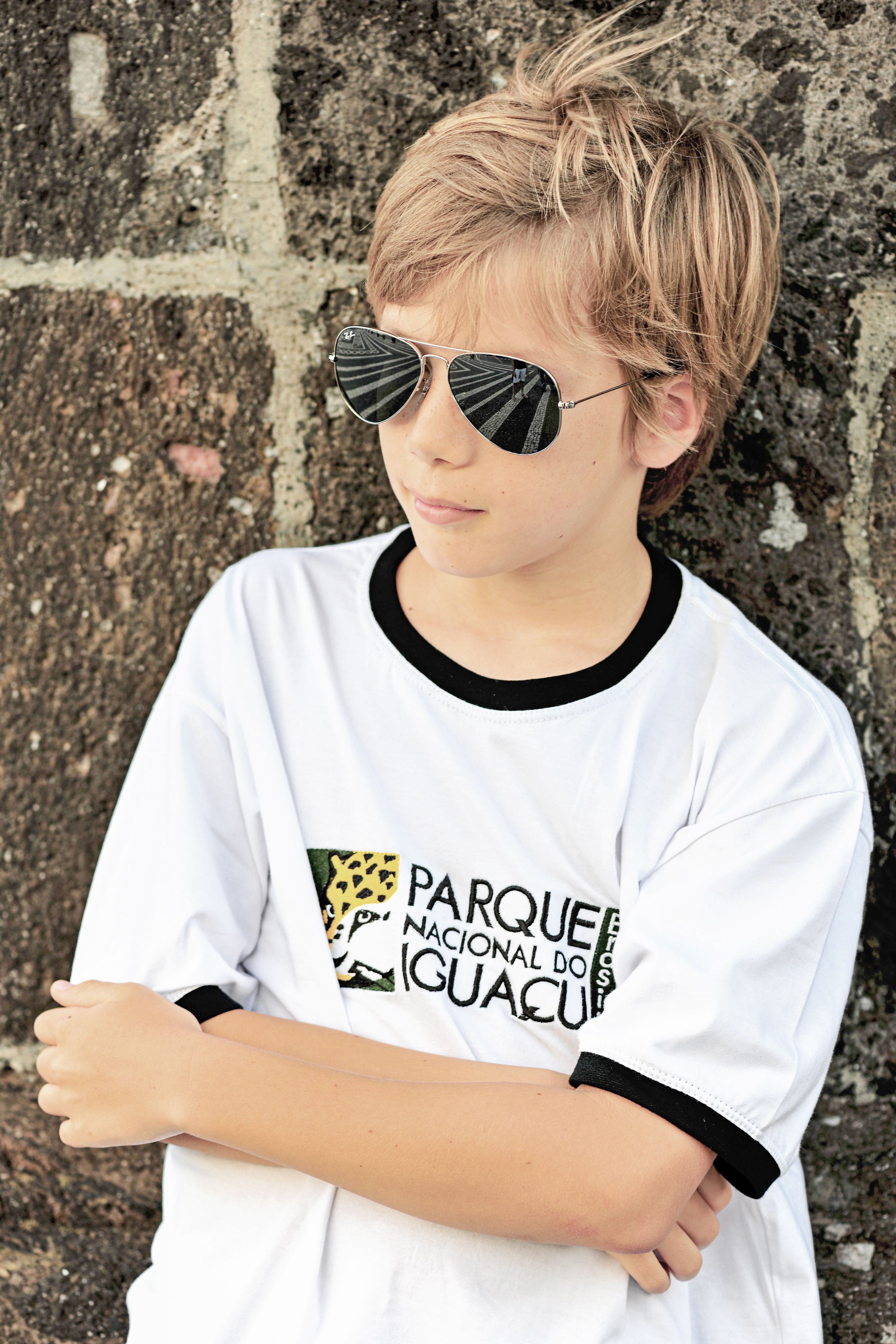 Portrait of a boy with sunglasses standing against a wall, displaying cool fashion style.