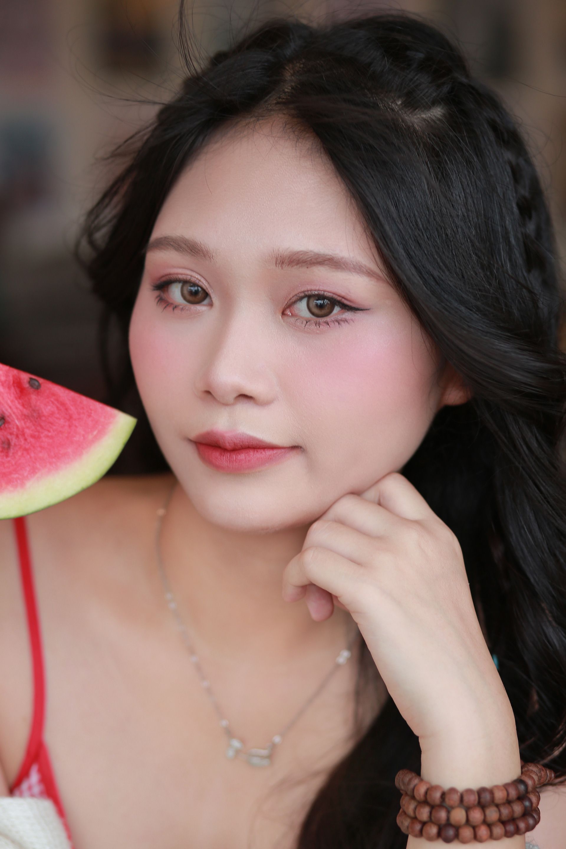 Beautiful woman with watermelon slice in hand, showcasing vibrant makeup and jewelry.