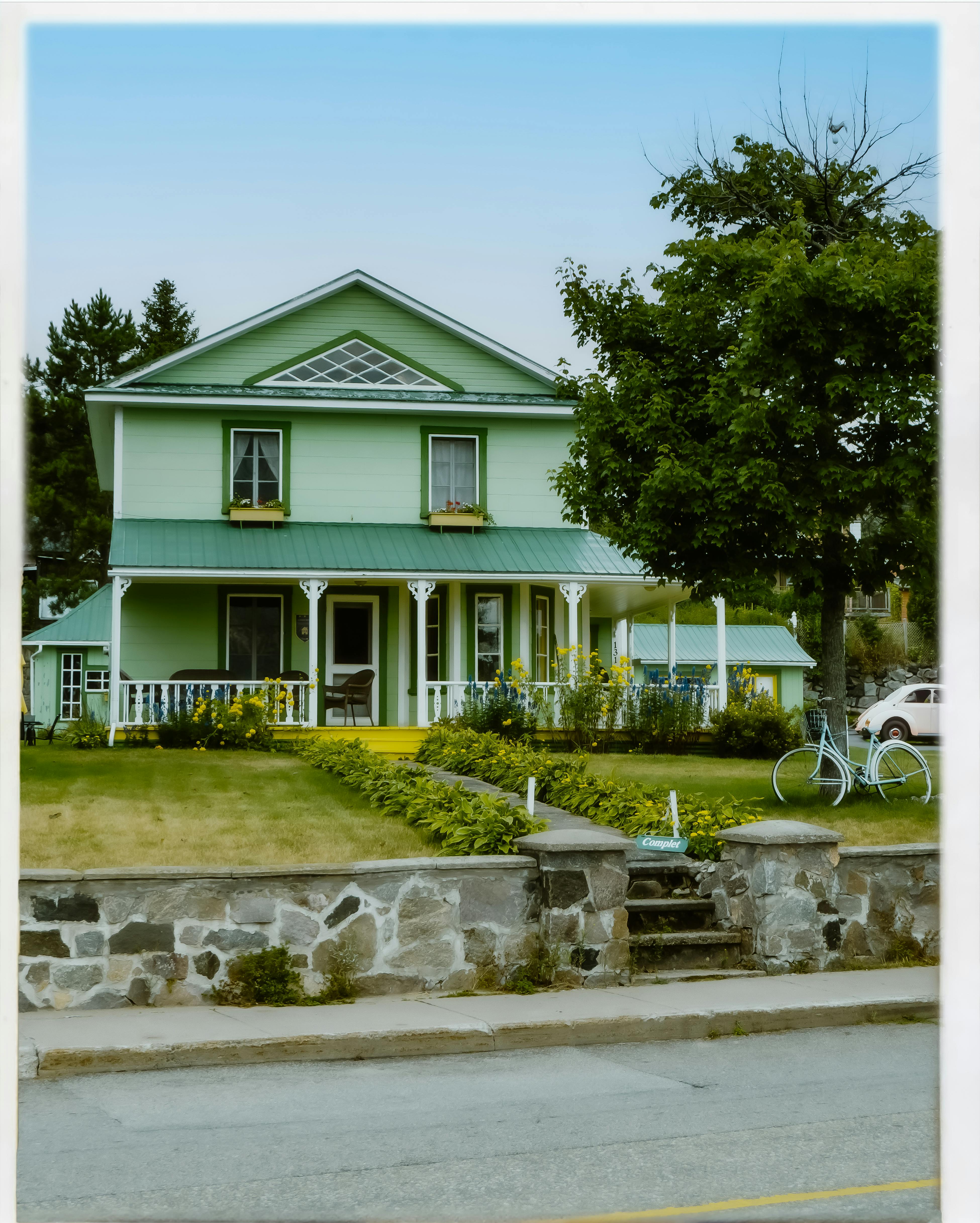 Quaint green house surrounded by lush garden in Tadoussac, Quebec, perfect for urban architecture exploration.