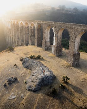 Dramatic aerial view of the Arcos del Sitio aqueduct under warm sunset light in Tepotzotlán, Mexico.