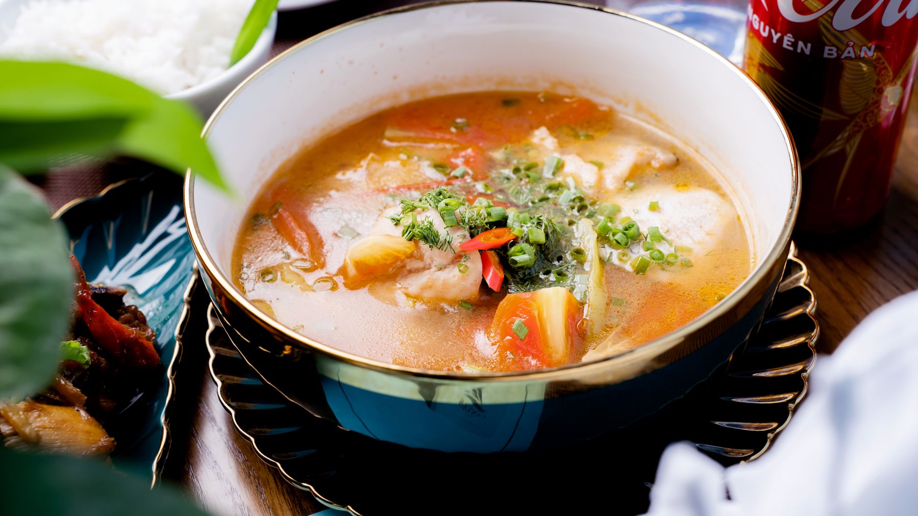 A colorful bowl of Asian fish soup garnished with fresh vegetables and herbs.