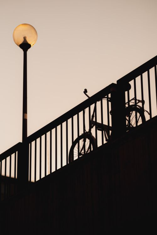 Free Moody silhouette of a bike against a fence at dusk with a street lamp glowing. Stock Photo