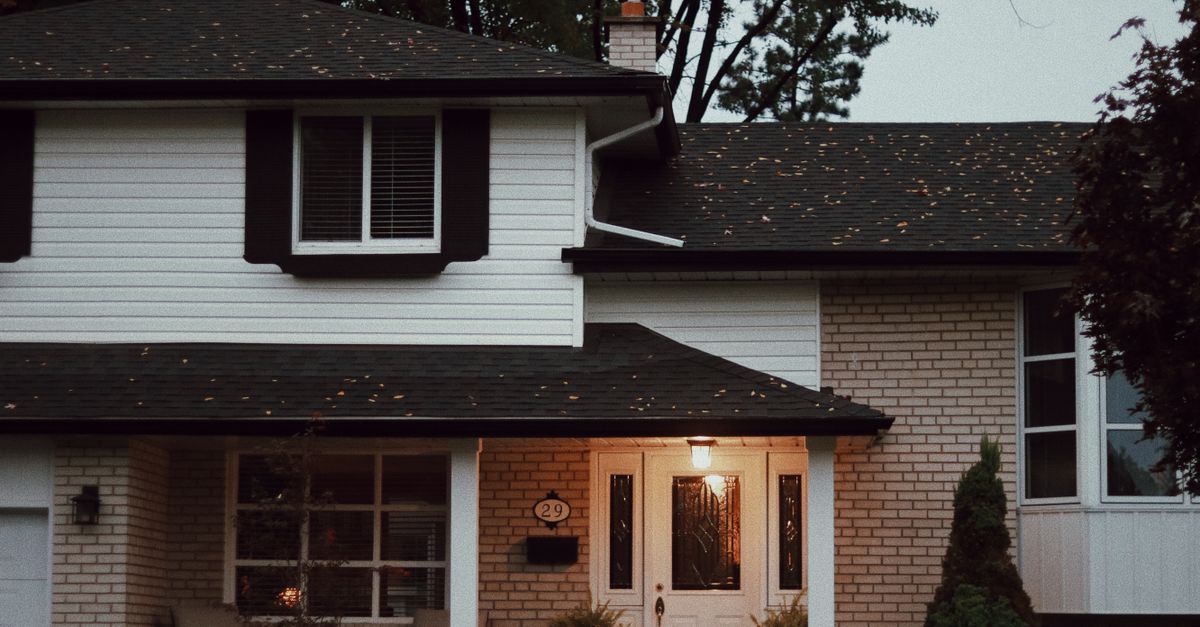 A cozy suburban house with a welcoming porch and lush potted plants at dusk.