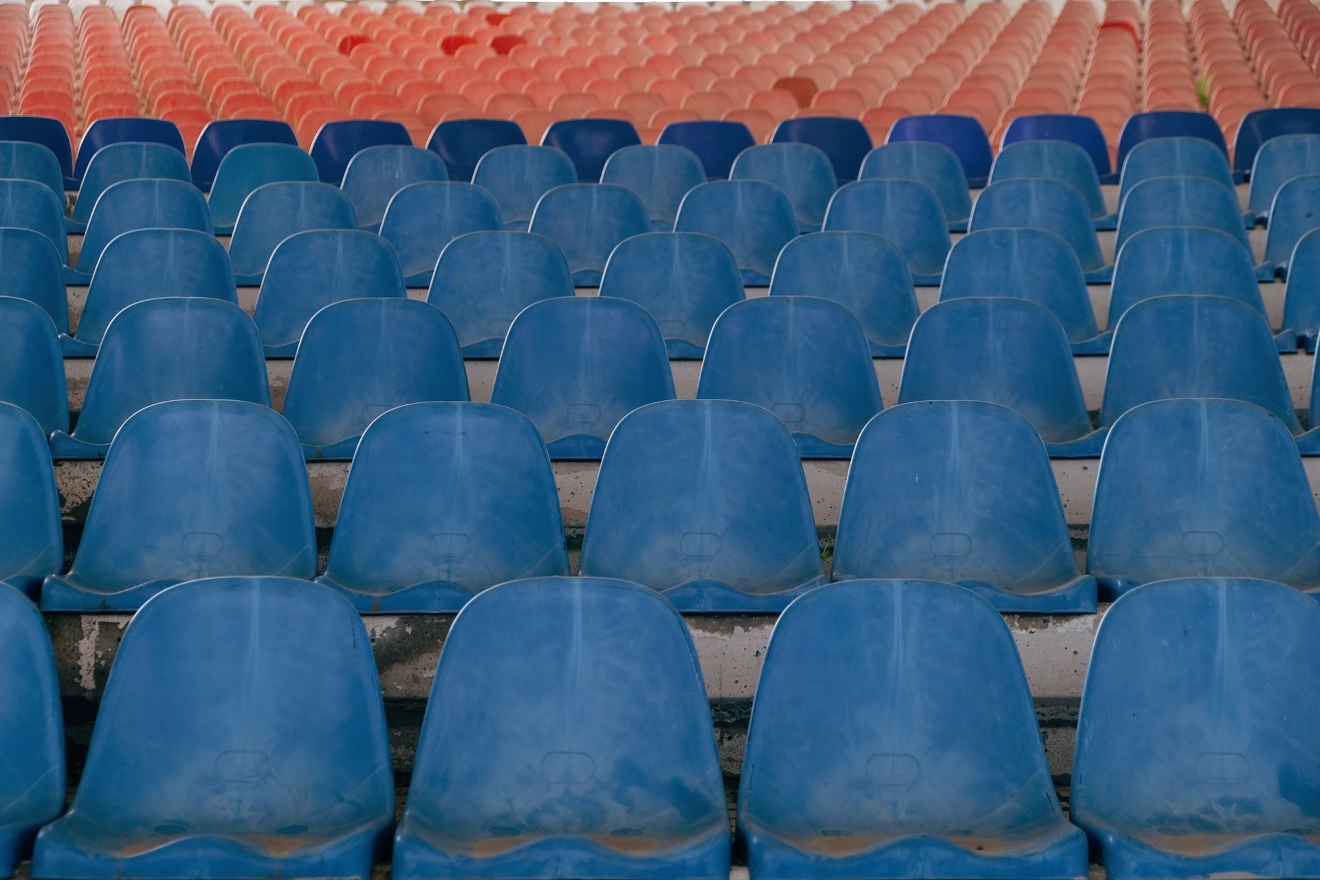 Rows of empty blue plastic seats in an outdoor stadium setting.