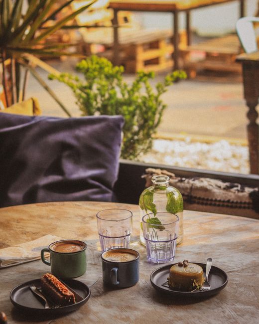 Warm indoor café scene with cappuccino, desserts, and glass water bottle on table.