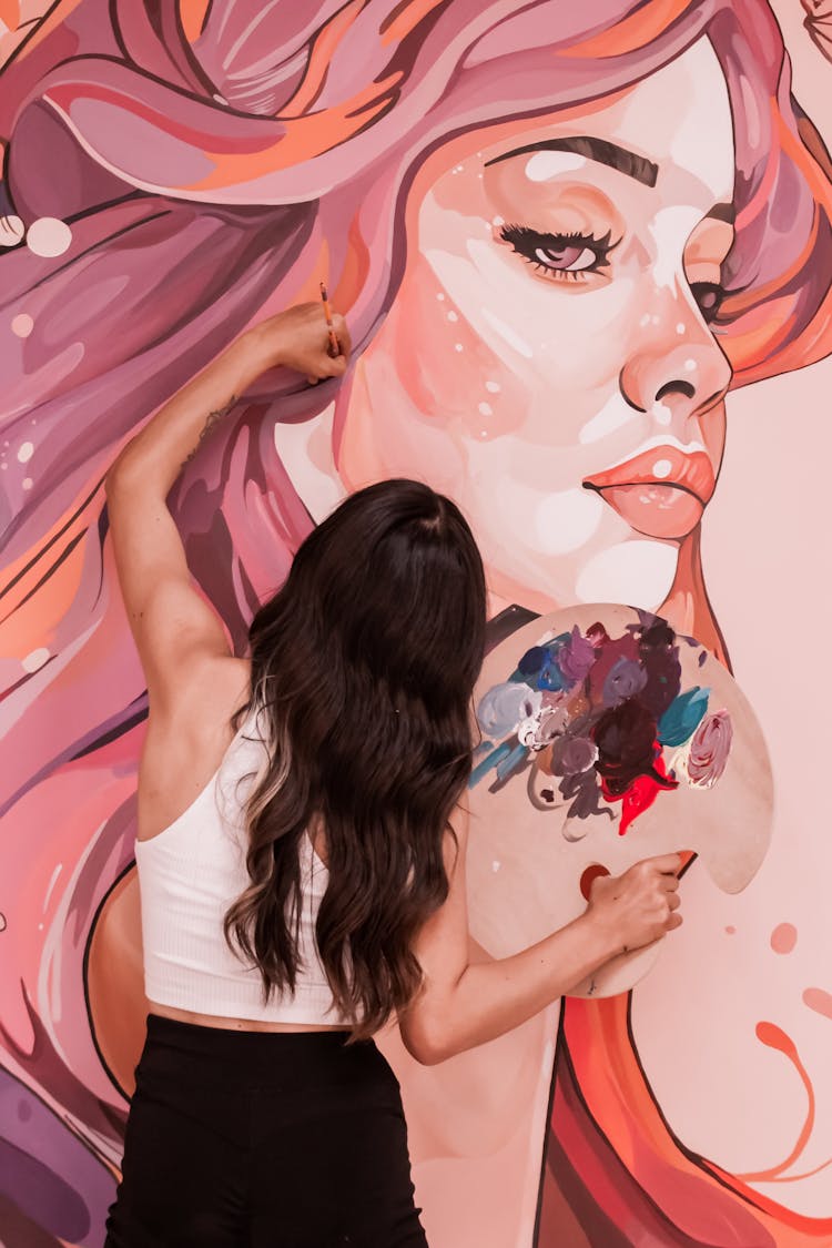 Back View Of A Woman Painting A Mural On A Wall 