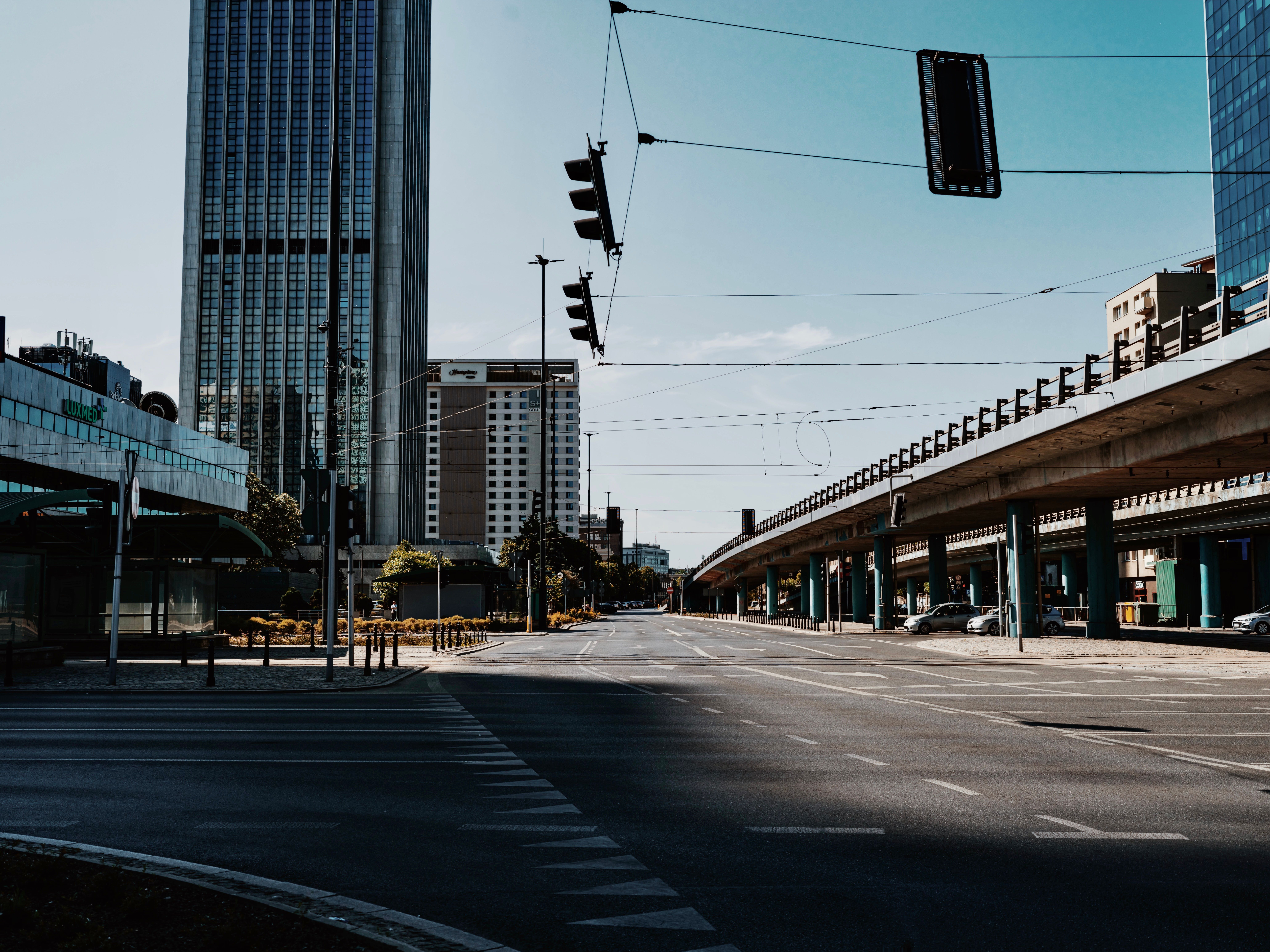 Wide sector road in Noida with the Blue Line viaduct, glass office towers and a mall entrance