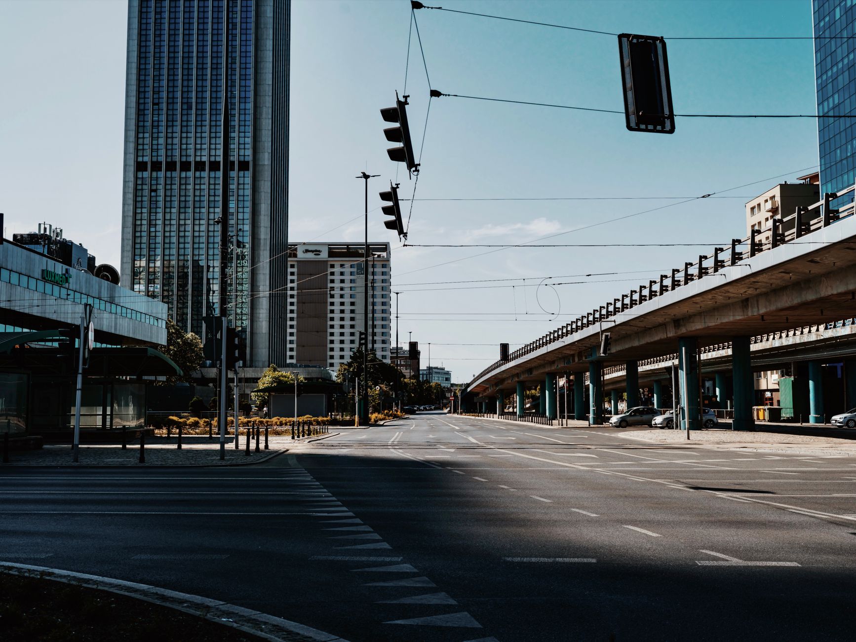 Wide sector road in Noida with the Blue Line viaduct, glass office towers and a mall entrance