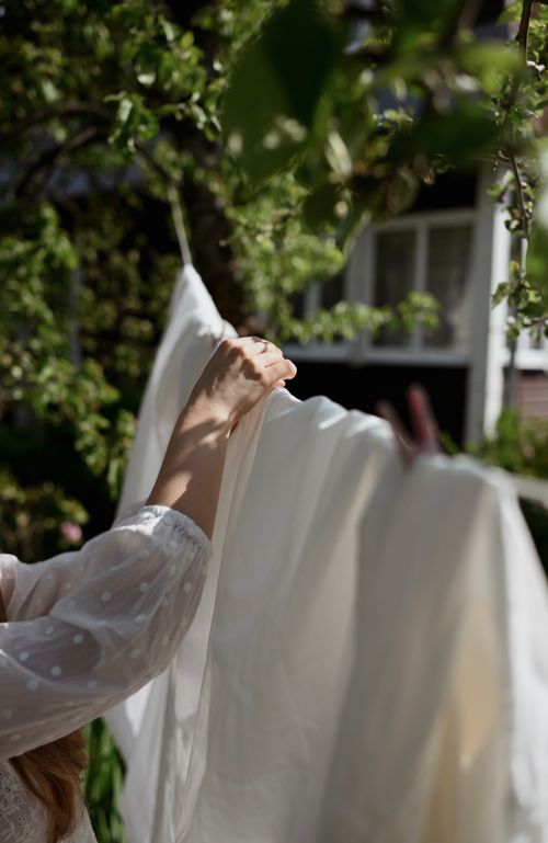 Free Close-up of a woman hanging a white bed sheet outdoors, capturing the essence of summer laundry day. Stock Photo
