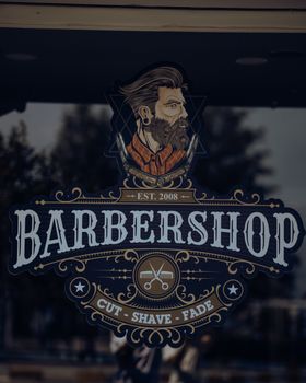 Detailed vintage barbershop logo featuring a bearded man on a reflective glass window. 17132124