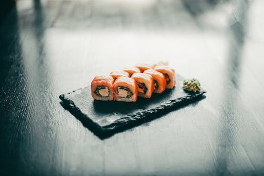 Close-up of salmon sushi rolls on a black slate, garnished with wasabi.