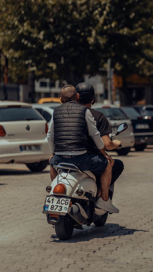 Free Two men riding a scooter through city streets on a sunny day, capturing urban lifestyle. Stock Photo
