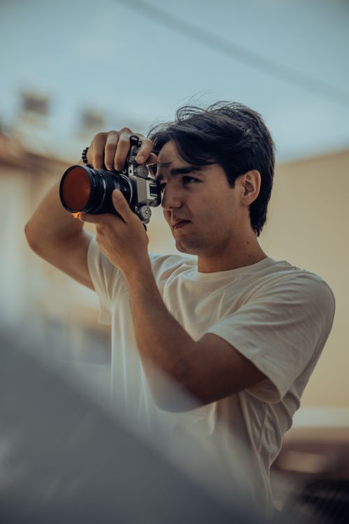 Free A young adult man taking photos with a camera outdoors. Stock Photo