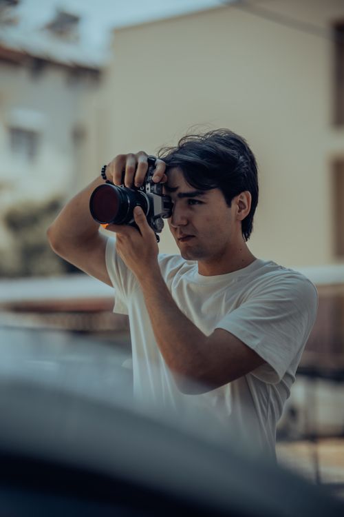 Free A young man in a white t-shirt using a vintage camera outdoors, capturing the moment. Stock Photo