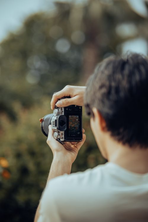 Free A man focuses his DSLR camera on a natural scene, blending technology with outdoor photography. Stock Photo