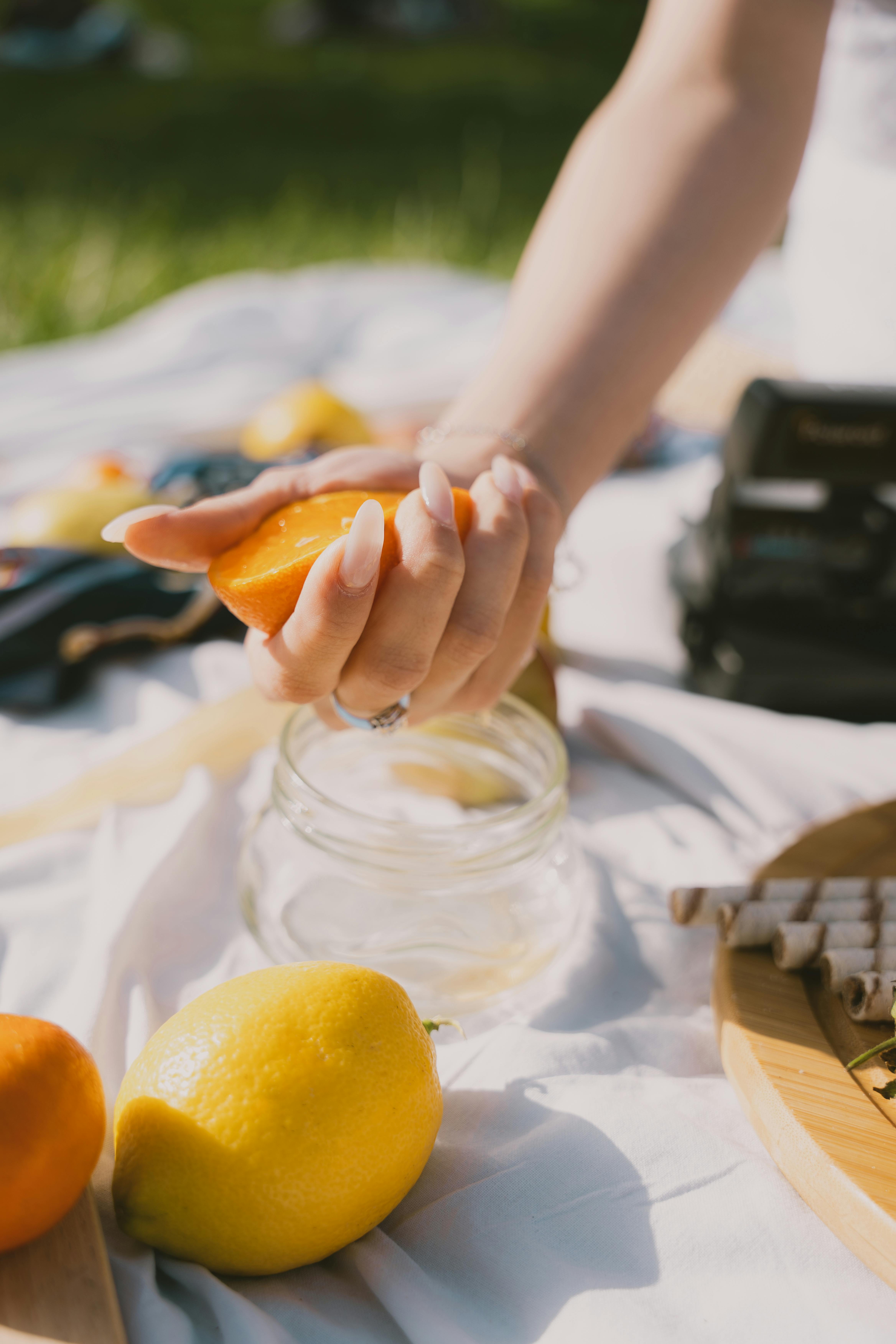 Enjoy a vibrant outdoor picnic with fresh lemons and oranges being squeezed into a jar. Perfect summer vibes.