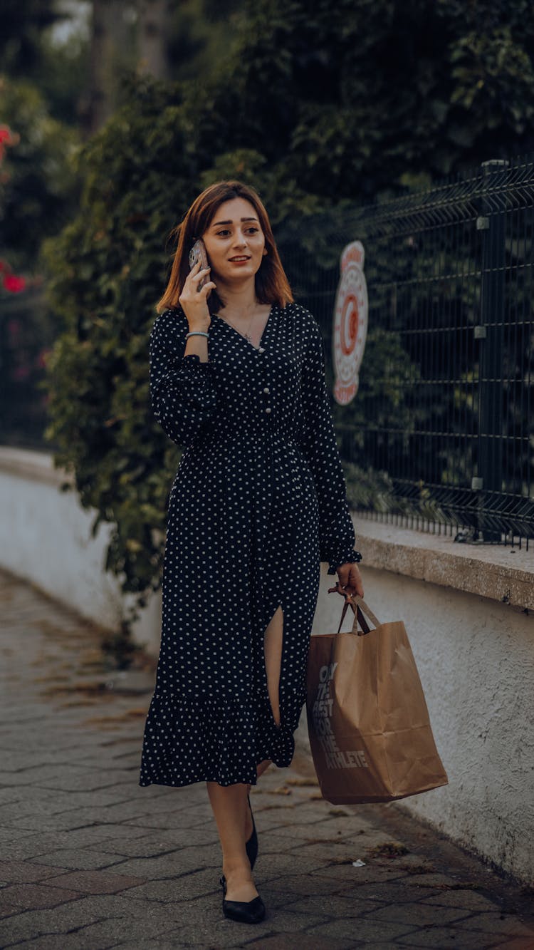 Young Woman In A Dress Walking On The Pavement And Talking On The Phone 