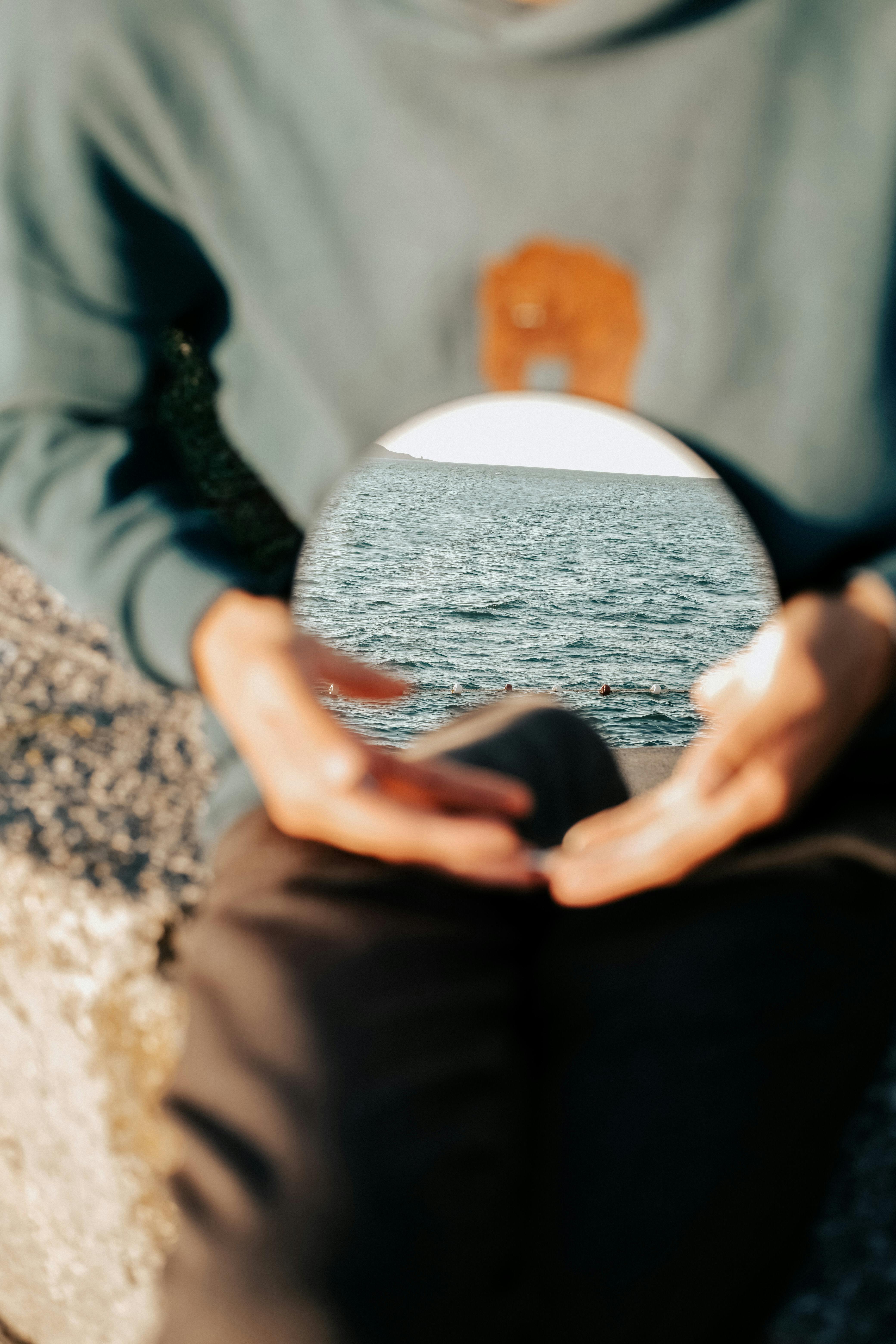 Creative shot capturing a sea reflection in a handheld mirror with blurred person.