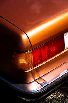 Detailed view of a vintage car's orange taillight and body in sunlight.