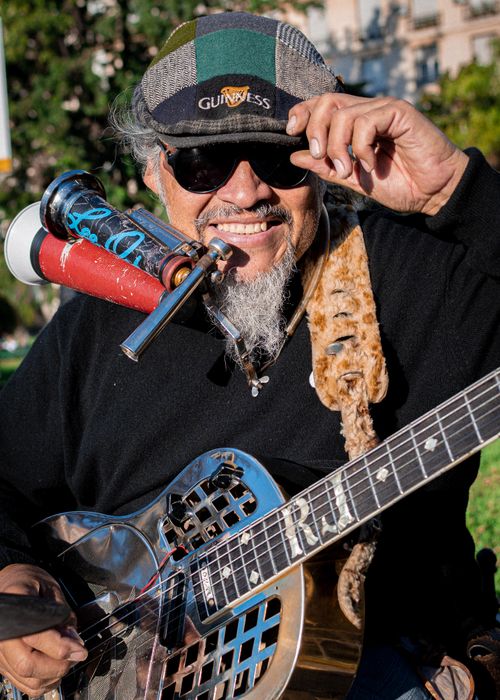 Free Smiling elderly musician in Buenos Aires playing guitar outdoors wearing sunglasses and cap. Stock Photo
