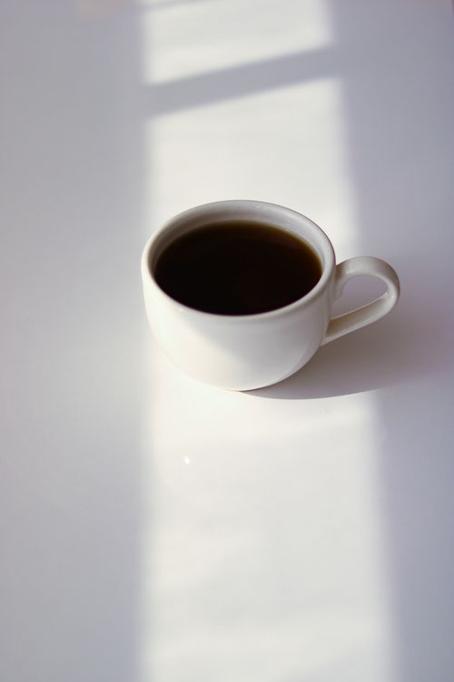 Free A serene minimalist shot of a coffee cup casting a shadow on a white table. Stock Photo