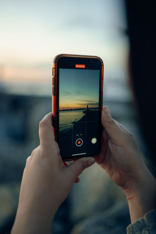 Free Female hands holding a smartphone capturing a beautiful sunset over the ocean, highlighting technology and nature. Stock Photo