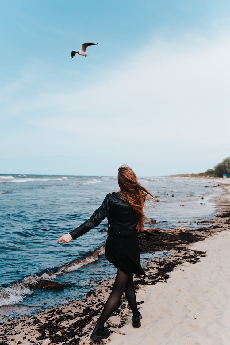 Back View Of A Woman In A Black Outfit Walking On The Beach 