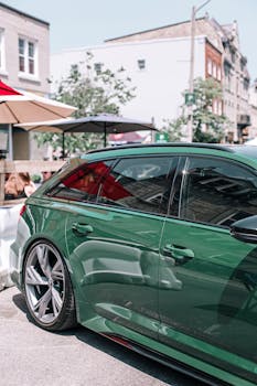 A glossy green sports car parked on a sunny urban street with a modern town backdrop.