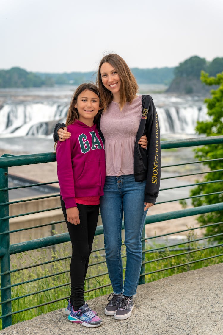 Mother And Daughter Posing In Front Of A Waterfall 