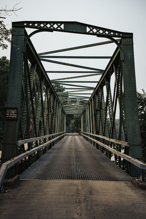 Free Vertical shot of an industrial green metal truss bridge under a clear sky with surrounding trees. Stock Photo